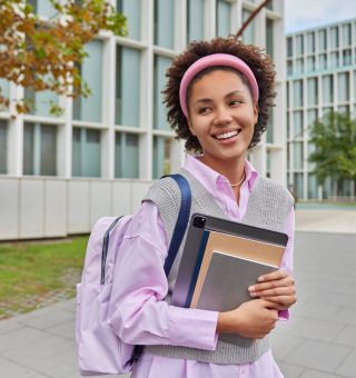 Jovem na frente da universidade com cadernos em seu colo