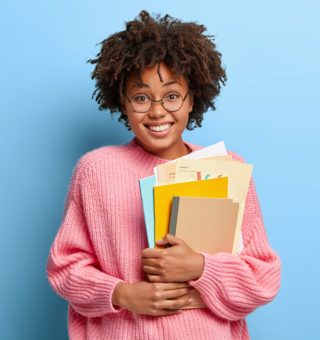 jovem universitária sorridente segurando cadernos nos braços após aprovação no Vestibular Social 2024