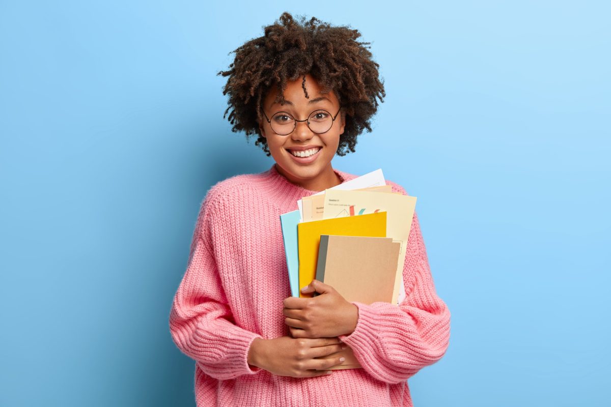jovem universitária sorridente segurando cadernos nos braços após aprovação no Vestibular Social 2024