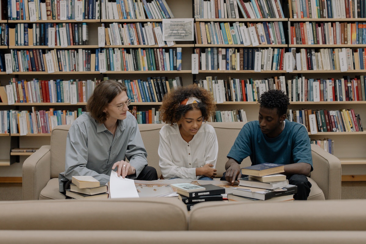 Três jovens sentados lendo em uma biblioteca