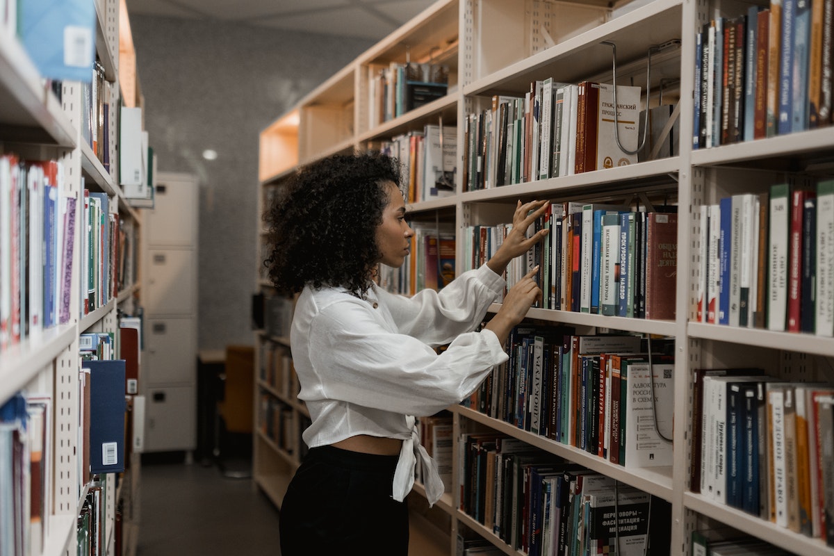 Uma aluna escolhendo um livro no corredor da biblioteca