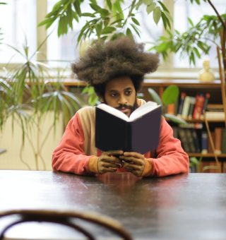 Aluno sentado em uma mesa lendo um livro de capa preta