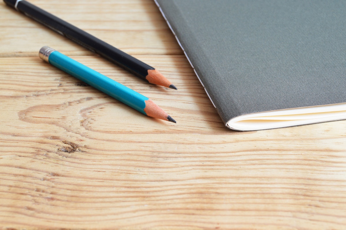 Dois lápis e um caderno em cima da mesa