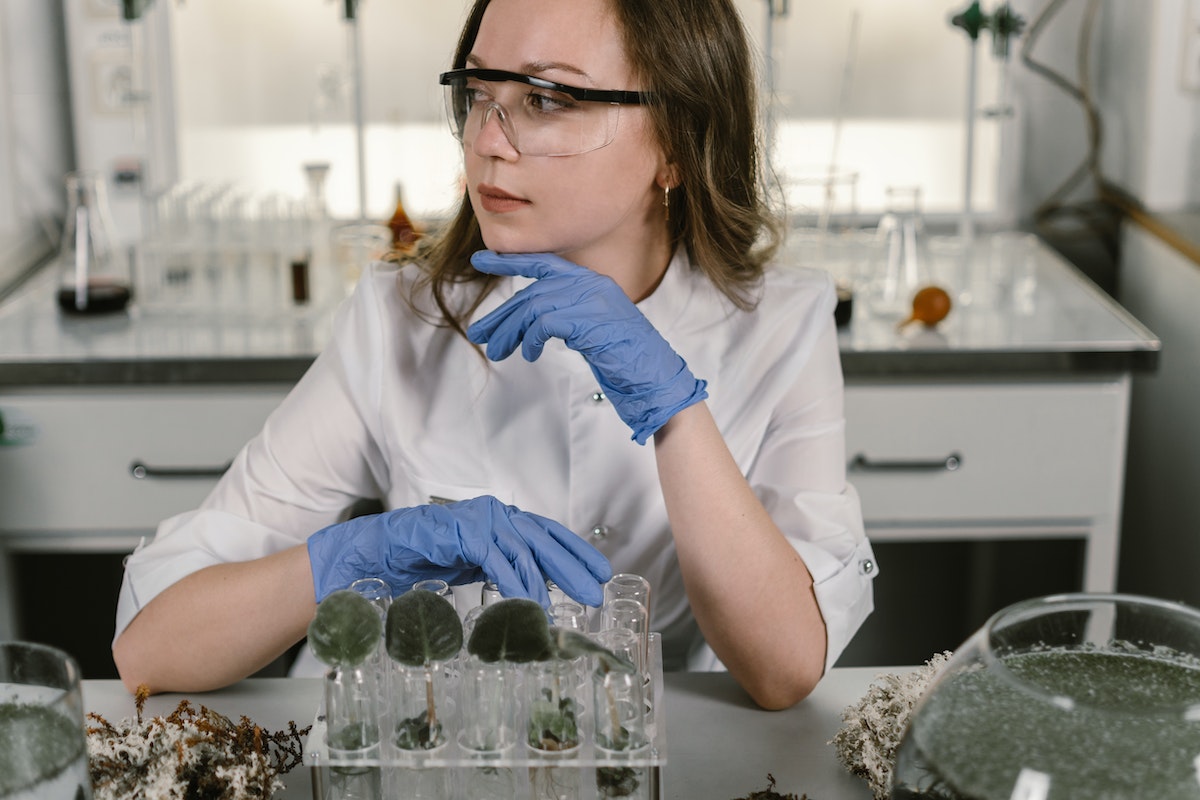 Estudante de biologia dentro do laboratório. Ela está com luvas de borracha azul e óculos de proteção