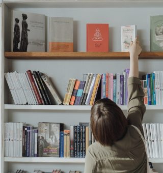 Uma estudante de Vestibular História 2024 na estante, pegando um livro