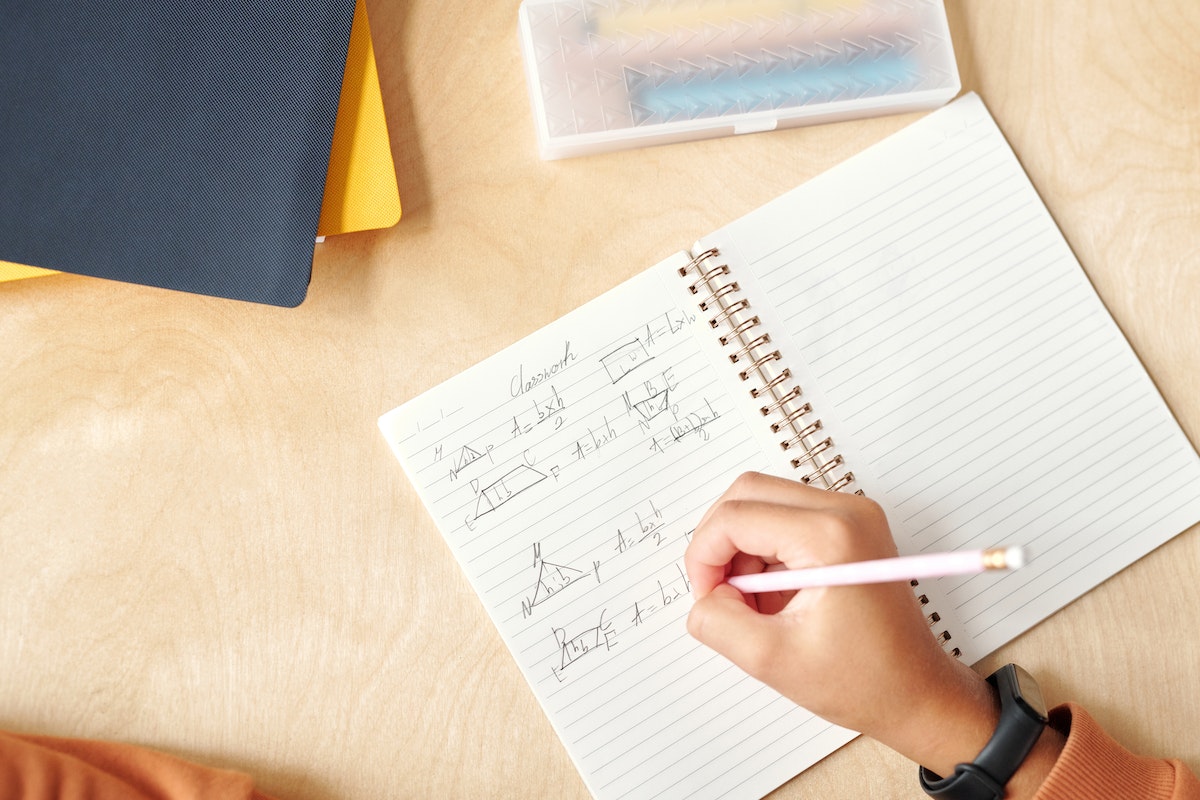 Vista de cima de uma menina escrevendo em um caderno com caneta azul