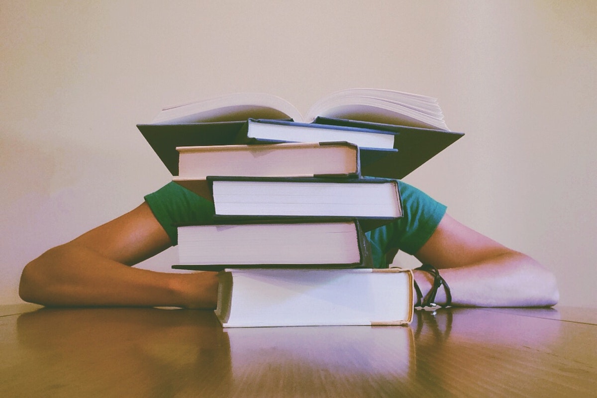 Um estudante com a cabeça abaixada, que está coberta por uma pilha de livros
