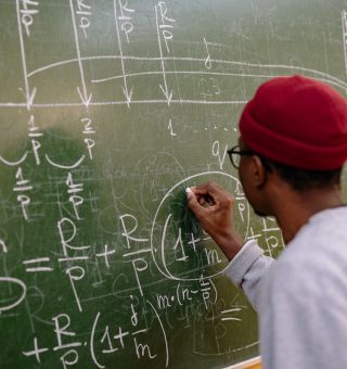 Um aluno de costas escrevendo na lousa de giz a solução de atividades de matemática