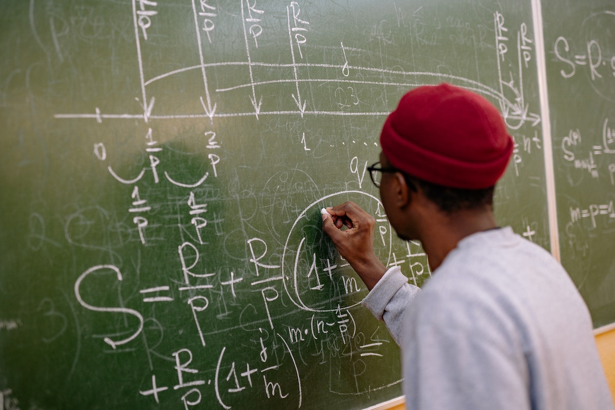 Um aluno de costas escrevendo na lousa de giz a solução de atividades de matemática