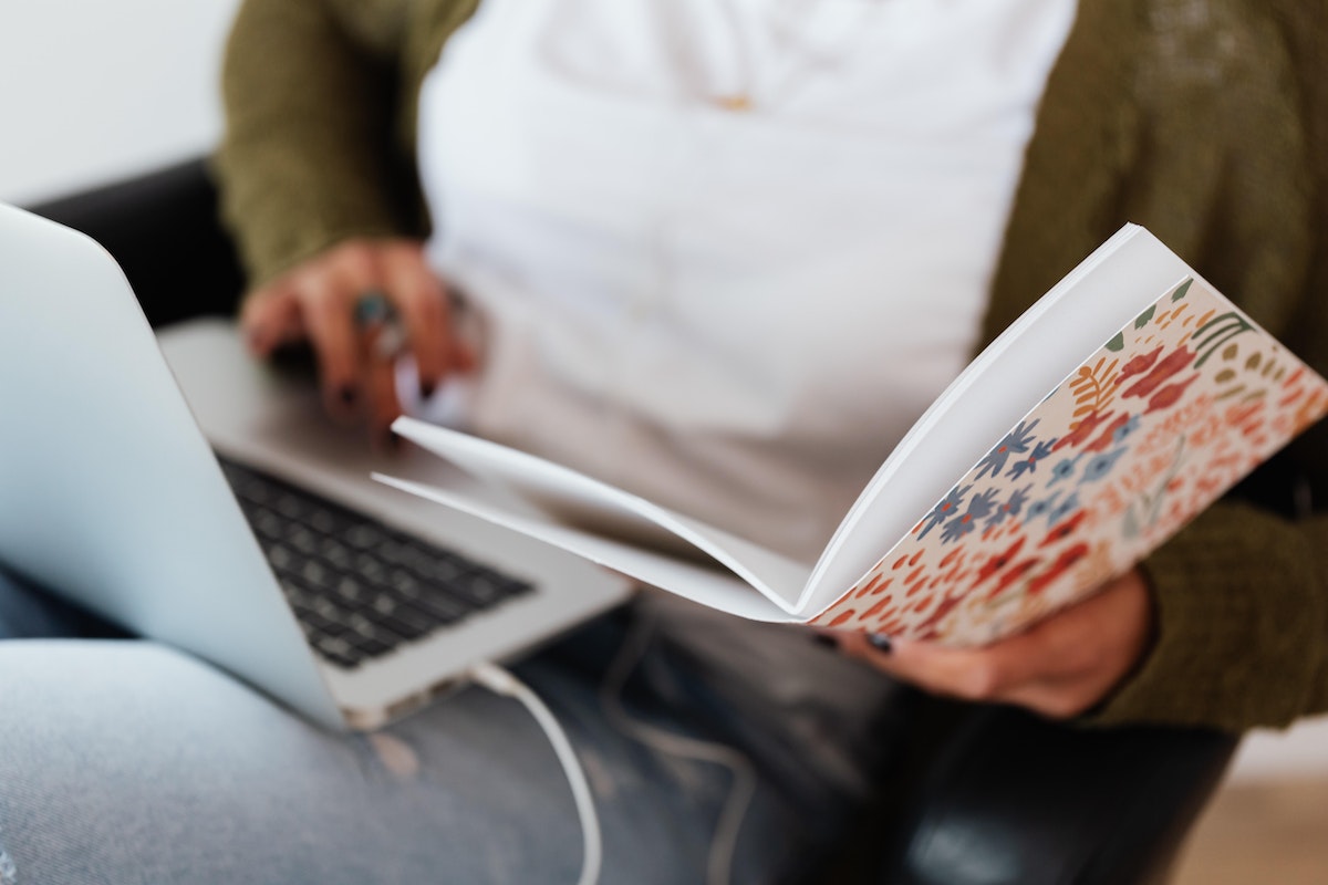 Uma mulher está com o notebook no colo e um caderno enquanto estuda para o Vestibular Unicuritiba 2024