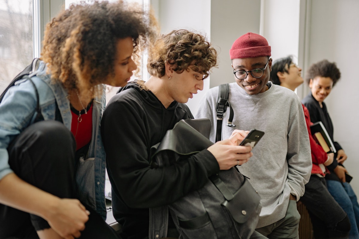 Um grupo de alunos está reunido em um lado e olham atentamente para o celular de um amigo