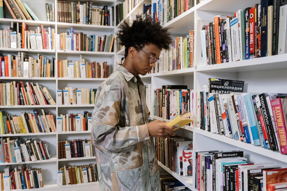 Um jovem está se preparando para o Sisu 2024. Ele está de pé em uma biblioteca com o livro aberto em sua mão