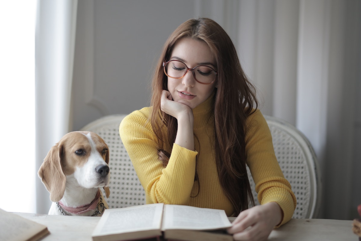 Uma estudante está do lado do seu cachorro. Ela lê um livro indicado para o Vestibular Santa Casa 2024