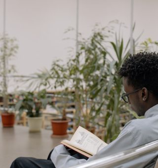 Um aluno está lendo um livro sentado, ao fundo há diversas plantas