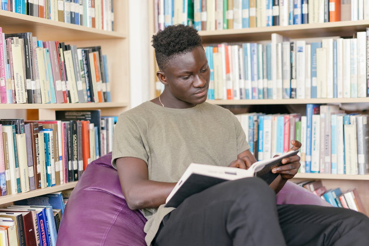 Um aluno está sentado em um Puff dentro de uma biblioteca enquanto lê um livro