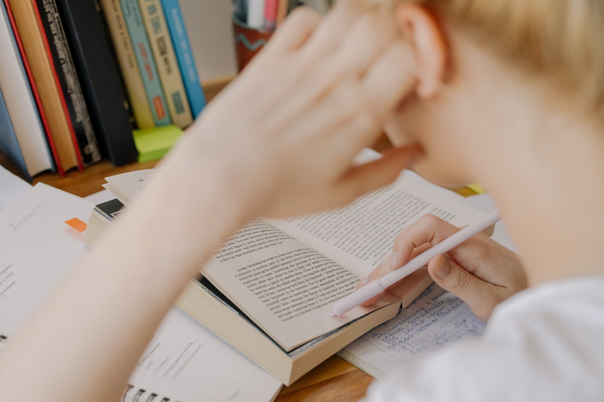 Um aluno está lendo um livro com a cabeça apoiada na mão e o cotovelo apoiado na mesa