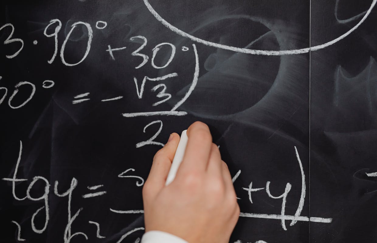 Uma pessoa escreve com um giz branco algumas fórmulas matemáticas em um quadro negro