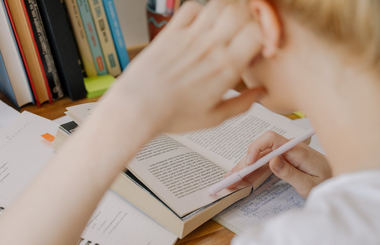 Um aluno está lendo um livro com a cabeça apoiada na mão e o cotovelo apoiado na mesa