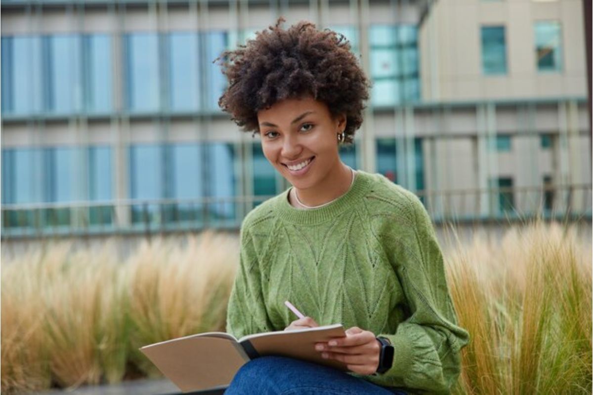 Uma aluna sentada ao ar livre. Ela faz anotações em seu caderno sobre as 9 Melhores Vestibulares RJ 2024