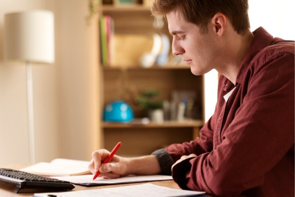 Um aluno sentado enquanto escreve em um caderno. Ele está estudando para o Vestibular Unificado 2024