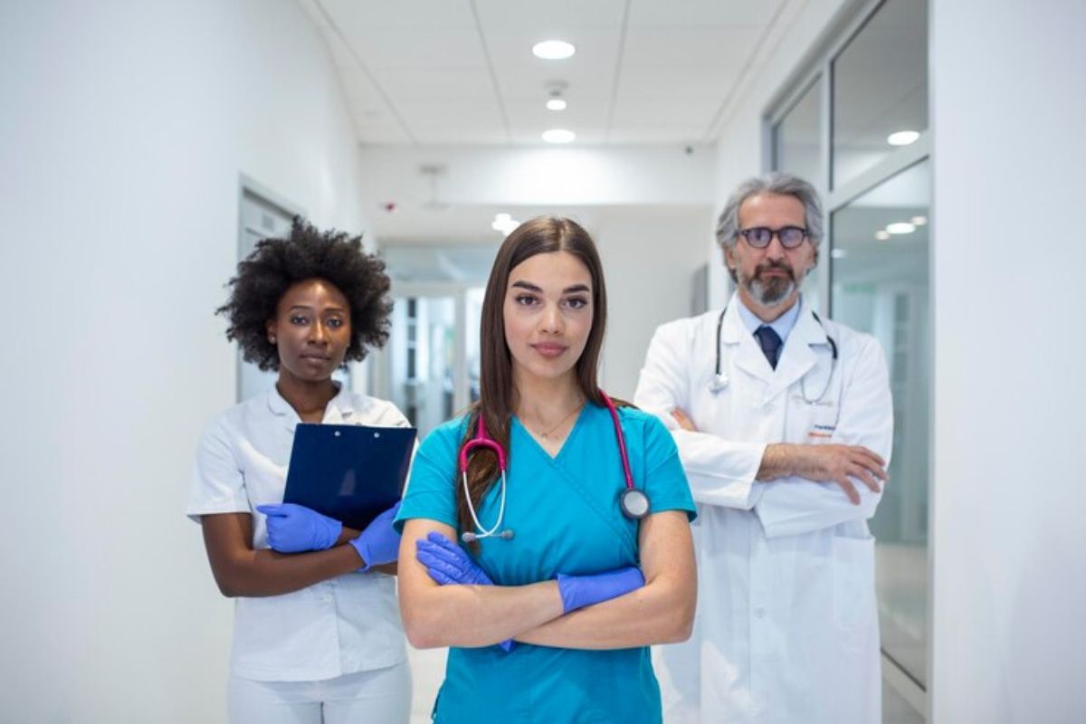 Três médicos. A aluna que está à frente veste uma roupa azul